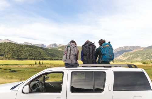 three people with backpacks sitting on top of a white SUV with the Colorado Front Range in the background