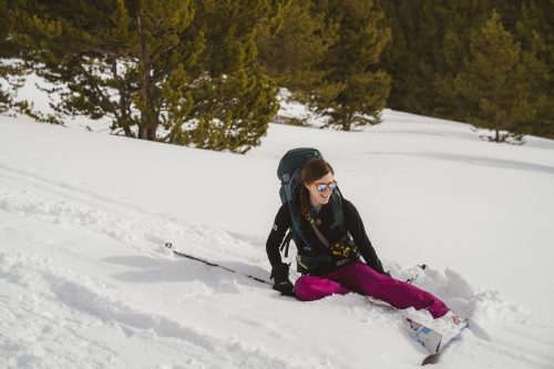 smiling woman wearing a pack and skiis sitting in snow